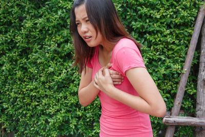 Young woman with chest pain standing against plants