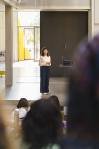 Full length of teacher explaining while standing in lecture hall at university