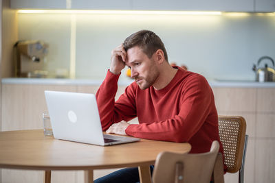 Sad frustrated man procrastinating after fired from job looking at laptop screen on kitchen at home.