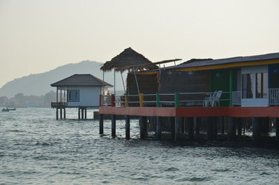 Stilt house on sea by buildings against clear sky