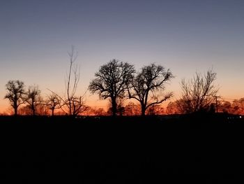 Silhouette bare trees on field against clear sky at sunset