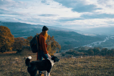 Rear view of woman with dog on mountain against sky