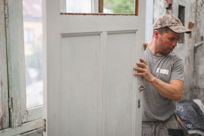 A young man holds an old door with both hands.