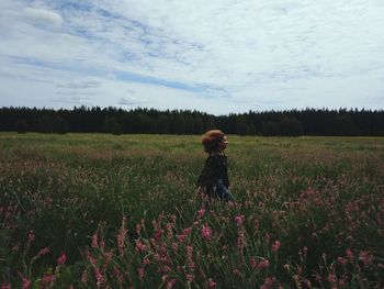 Side view of young woman walking on grassy field against sky