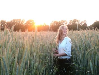 Happy woman standing amidst wheat field against sky during sunset