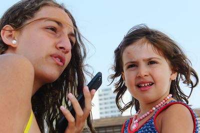 Close-up of sisters talking on phone against clear sky