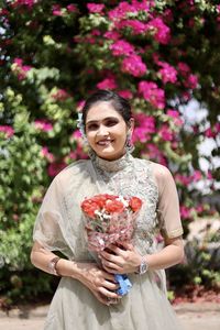 Smiling young woman holding flower bouquet against plants