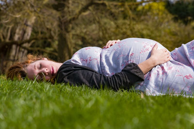 Side view of pregnant woman lying on field at park
