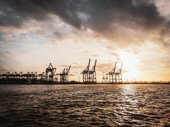 Cranes at commercial dock against sky during sunset