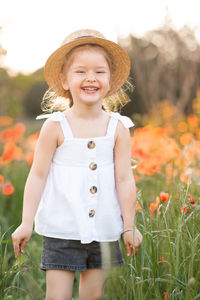 Portrait of cheerful girl wearing hat on flowering field