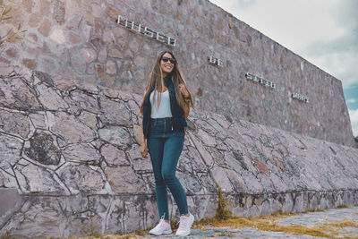 Full length of young woman standing against wall