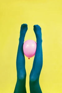 Low section of person holding pink balloon against yellow background