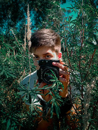 Portrait of boy holding plants against trees