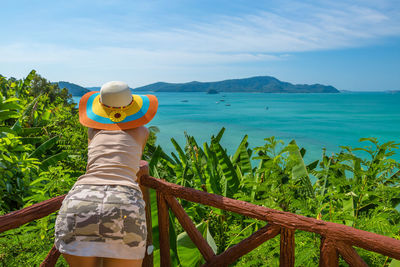 Rear view of woman leaning on railing by sea against sky