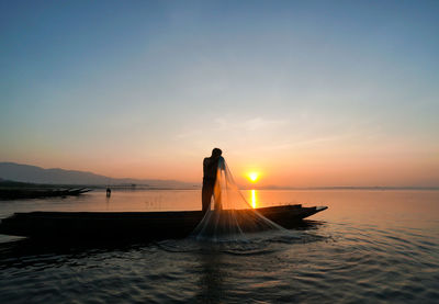 Silhouette man standing in sea against sky during sunset