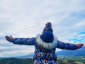 Rear view of girl with arms outstretched against cloudy sky