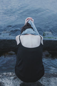 Rear view of woman holding scarf while sitting by sea