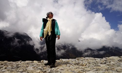 Low angle view of woman standing on mountain against cloudy sky