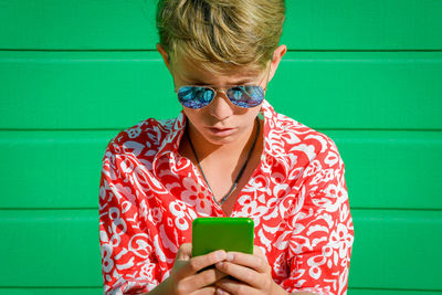 Boy wearing sunglasses using mobile phone against wall