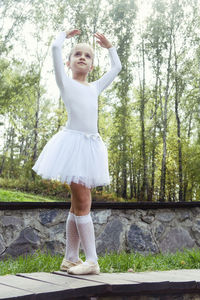 A little ballerina girl shows elements of choreography on a summer day on a path in the park