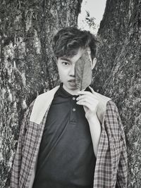 Portrait of young man standing against tree trunk