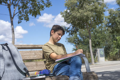 Boy writing in book while sitting on bench