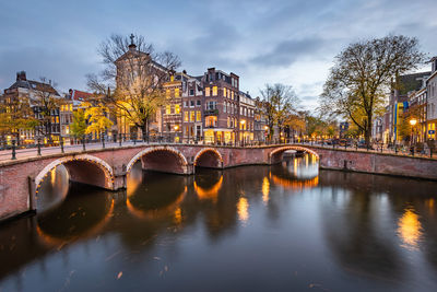 Bridge over river by buildings against sky in city