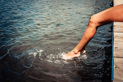 Unrecognizable woman's legs splashing water while relaxing on a pier in summer.