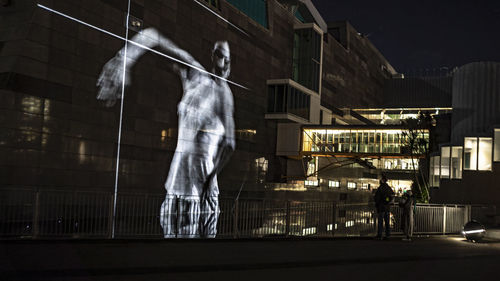 People standing on street against illuminated buildings in city at night