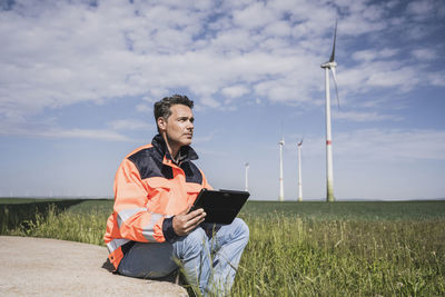 Engineer with tablet pc sitting near wind turbine on field