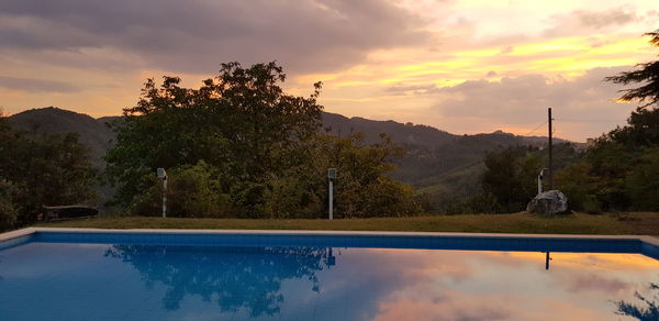 Reflection of trees in swimming pool against sky during sunset