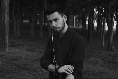 Portrait of young man standing against trees in forest