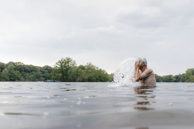 Senior man in a lake splashing water in his face