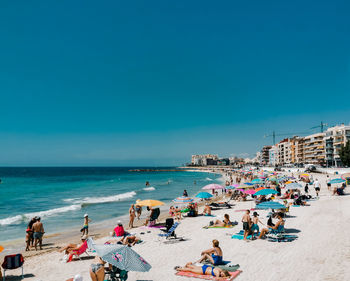 People at beach against clear blue sky