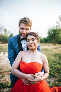 Smiling newlywed couple embracing on field against sky