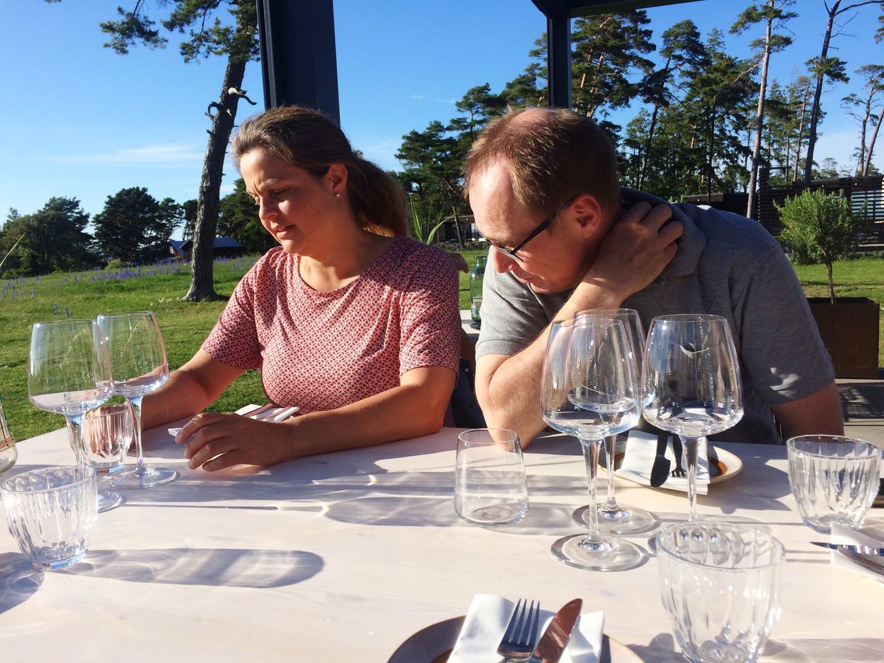 table, wineglass, place setting, food and drink, drinking glass, plate, two people, drinking water, dining table, real people, restaurant, water, togetherness, outdoors, drink, day, young adult, wine, tree, young men, fork, sitting, young women, lifestyles, food, sky