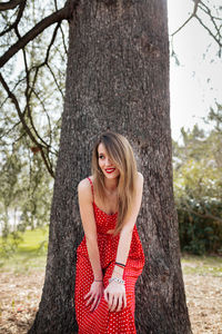 Smiling woman looking away while leaning on tree trunk in park