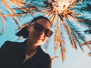 Close-up portrait of young woman wearing sunglasses against sky