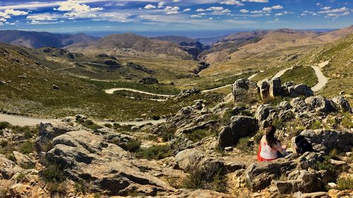 Rear view of woman sitting on rock against cloudy sky