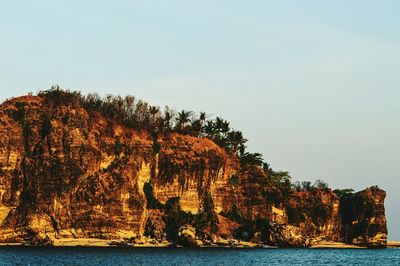 Rocks in calm sea against clear sky