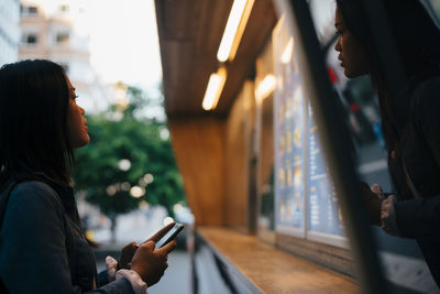 Side view of teenage girl standing with mobile phone while looking at menu