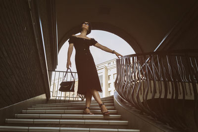 A pretty charming middle-aged woman in a black dress and sunglasses strolls through in the stairs
