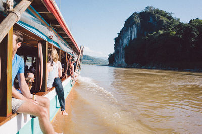 Passengers traveling in ferry over river against mountain