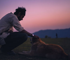 Man with dog sitting against sky during sunset