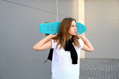 Portrait of young woman standing against wall