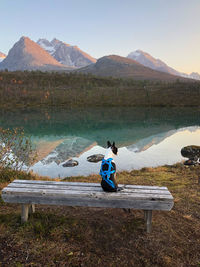 Rear view of man sitting on lake against mountains