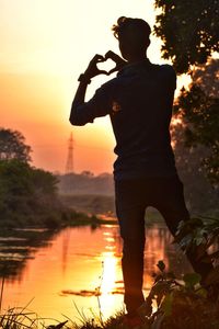 Silhouette man photographing by lake against sky during sunset