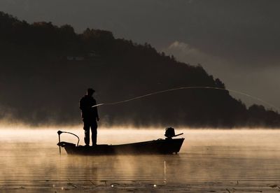 Silhouette man fishing in lake against sky