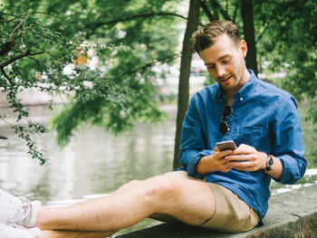 Young man using phone while sitting on tree