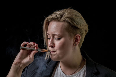 Close-up of young woman smoking over black background